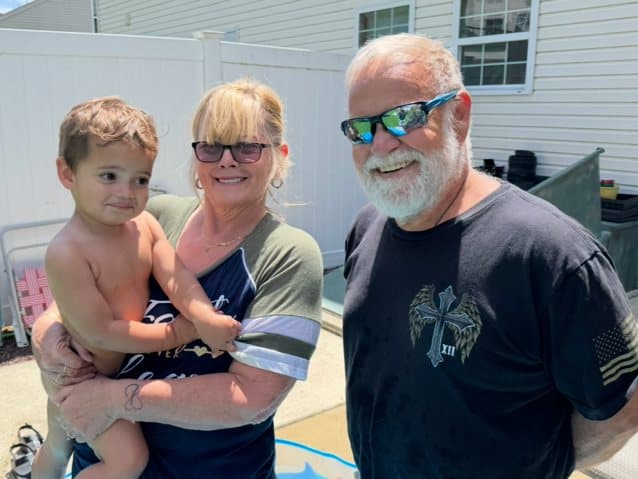 Two adults holding a young child in a sunny backyard